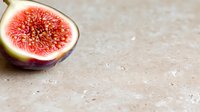 Fresh ripe fig cut in half showing vibrant pink flesh and seeds on light stone background with copy space for food photography and design.