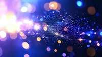 Magical glowing particles and bokeh lights on dark blue background create dreamy atmosphere with sparkling dust and blurred circles for festive designs.