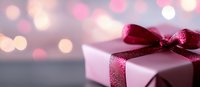 Pink gift box with burgundy ribbon bow against blurred festive bokeh background in soft pastel colors, creating romantic holiday atmosphere.