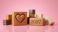 Wooden blocks with heart symbol and 2027 text arranged on pink background, representing love, new year goals, future planning and positive aspirations for design projects.