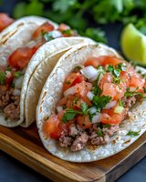 Mexican street tacos with seasoned ground beef, fresh pico de gallo, chopped onions, and cilantro on soft corn tortillas served on wooden cutting board.