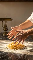 Chef hands kneading fresh pasta dough on marble counter in warm sunlit kitchen for authentic Italian cooking and culinary preparation.