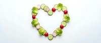 Fresh vegetables arranged in heart shape on white background, featuring cucumber slices, radishes and broccoli florets. Concept for healthy eating, nutrition and diet.