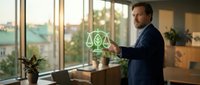Professional businessman in dark suit using tablet with digital justice scales hologram in modern office environment during golden hour lighting.