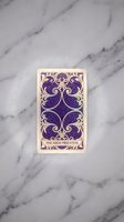 Ornate purple tarot card with intricate golden baroque patterns on white marble surface for mystical divination and spiritual guidance practices.