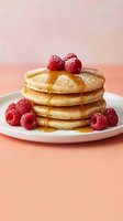 Stack of fluffy pancakes topped with fresh raspberries and golden syrup on white plate against soft pink background for breakfast menu design.