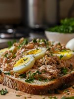 Open-faced sandwich with tuna salad and sliced hard-boiled eggs on rustic bread, garnished with fresh herbs in modern kitchen setting for healthy meal concepts.