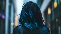 Young woman with vibrant blue dyed hair shown from behind against blurred urban nighttime background with bokeh lights creating moody atmospheric scene.