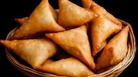 Freshly baked golden samosas arranged in woven basket, crispy triangular pastries with savory filling on dark background, traditional Indian appetizer.