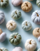 Pastel colored pumpkins in white, cream and sage green arranged on soft blue background creating modern autumn seasonal composition for holiday decor.
