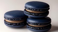 Dark blue macarons with chocolate filling stacked on neutral background. French pastry dessert cookies for bakery menu, culinary blog, food photography.