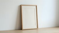 Empty wooden picture frame with white mat leaning against neutral wall on wooden surface, ready for artwork display and home decor projects.
