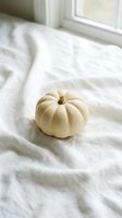 Small white pumpkin on rumpled bed sheets near window creating cozy autumn bedroom decor atmosphere for seasonal home styling and fall interior design.