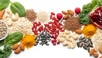Assorted superfoods including nuts, seeds, legumes, grains and leafy greens arranged on white background for healthy nutrition and wellness concepts.