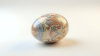 Decorative Easter egg with intricate swirl patterns in gold, blue and bronze colors on neutral background for holiday celebrations and spring decor.