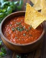 Fresh homemade salsa served in wooden bowl with crispy tortilla chips and herbs, closeup of traditional Mexican appetizer garnished with cilantro.