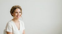 Young woman with blonde braided hair wearing white v-neck shirt, smiling at camera against neutral background. Isolated portrait for beauty, wellness, and lifestyle design projects.