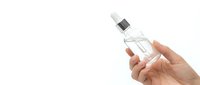 Hand holding clear glass perfume bottle with silver cap against white background for cosmetic and fragrance advertising.