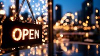 Illuminated open sign hanging in window with blurred city lights and bokeh background creating warm welcoming atmosphere for business establishments.