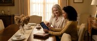 Two professional women collaborating on tablet computer in elegant home office setting with warm natural lighting and classic interior design.