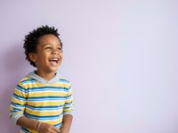 Young boy with dark curly hair and medium skin tone wearing yellow and blue striped shirt, laughing joyfully against lavender background. Suitable for children's clothing, parenting, education, and lifestyle marketing.