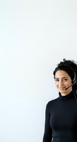 Young woman with dark hair and South Asian ethnicity wearing headset and black turtleneck, smiling at camera against white background. Customer service representative or telemarketer.