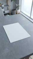 Blank white paper sheet on gray desk surface in modern office workspace for business presentations and creative projects.