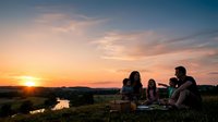 Family enjoying outdoor picnic at sunset with scenic landscape, golden hour lighting, and natural countryside setting for leisure and lifestyle content.