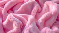 Soft pink plush fabric with gentle folds and waves creating luxurious texture. Close up view of cozy fleece material shows delicate light and shadow play.