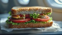 Fresh sandwich with lettuce, tomato, cheese and ham on toasted sesame bread, served on white paper. Close up view with natural lighting and soft background.