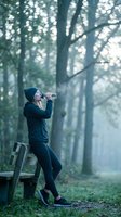 Young woman drinking water from bottle during outdoor workout break in misty forest park wearing athletic clothing and beanie hat for healthy lifestyle.