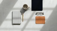 Modern workspace flat lay with coffee cup, tablet, notebook, glasses and leather wallet on white surface with natural shadows for business lifestyle design.
