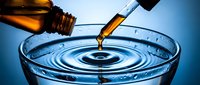 Amber liquid pouring from glass bottle into laboratory petri dish creating ripples. Scientific research, chemical analysis, pharmaceutical testing concept.