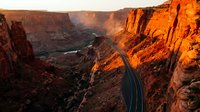Aerial view of winding desert highway through dramatic canyon landscape at golden hour, showcasing red rock formations and serpentine road for travel and nature content.