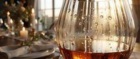 Elegant crystal whiskey glass with amber liquid on festive holiday table setting with warm bokeh lights and Christmas decorations creating luxurious atmosphere.