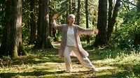 Senior woman practicing tai chi in peaceful forest setting for wellness and mindfulness exercise routine.
