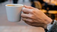 Unrecognizable person holding white ceramic mug with hot beverage, wearing casual clothing and wristwatch, suitable for lifestyle and beverage marketing.