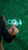 Hand pointing at glowing CO2 text with downward arrow against green natural background representing carbon dioxide reduction and environmental sustainability.