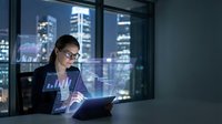 Professional businesswoman analyzing financial data on holographic displays in modern office at night with city skyline background for corporate presentations.