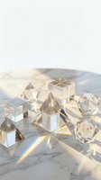 Clear crystal geometric shapes creating rainbow light reflections on marble surface for luxury design and meditation concepts.