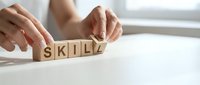 Professional hands arranging wooden blocks spelling skill on white surface, representing professional development, competency building, and career advancement for business training materials.