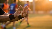 Construction worker's dirty hands cupped in prayer or gratitude gesture at sunset on building site with warm golden light and blurred colleagues in background.