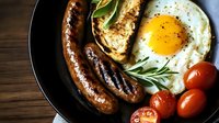 Hearty breakfast plate with grilled sausages, sunny side up egg, cherry tomatoes, fresh rosemary and toasted bread on dark cast iron pan. Rustic morning meal.