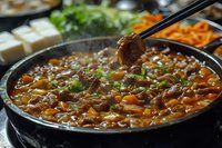 Korean beef stew with vegetables in black pot, chopsticks holding meat piece, traditional Asian comfort food with carrots and herbs for cooking blogs.