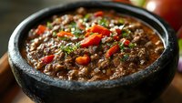 Hearty black bean soup garnished with fresh tomatoes and herbs in traditional stone bowl, rich texture and vibrant colors create appetizing Mexican cuisine.