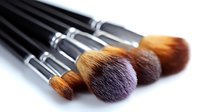 Professional makeup brushes with soft brown bristles and black handles arranged in diagonal composition on white background, isolated for beauty and cosmetic design.