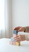 Woman hands building colorful wooden block tower on white table demonstrating balance and construction skills in bright minimalist interior.
