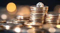 Small house model on stack of coins representing real estate investment and property financing with warm bokeh lights background.