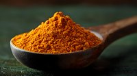 Ground turmeric powder heaped in wooden spoon against dark background, vibrant orange spice macro photography showing detailed texture and rich color.