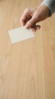 Senior male hand holding blank white card on wooden surface for business card mockup and branding presentation.